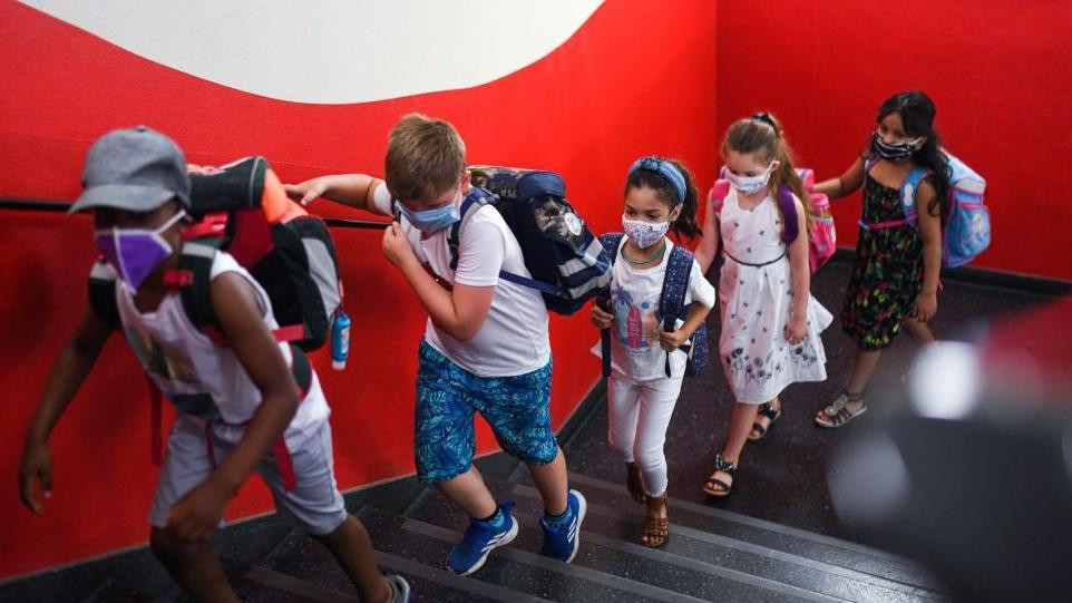 Deca sa maskama na licu penju se uz stepenice