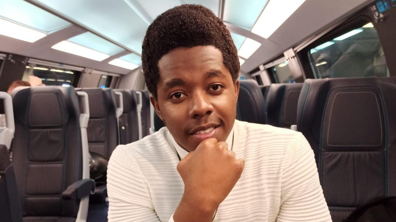 Glodi sedi u vozu Beograd-Novi Sad, obučen u belu rolku, rukom podupire bradu, Kongo, rat u Kongu, rat u Demokratskoj Republici Kongo