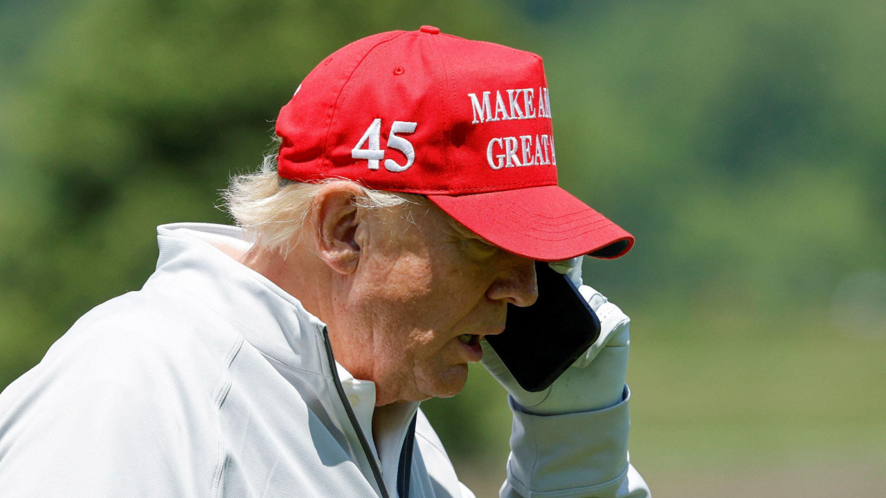 Donald Trump u beloj jakni i sa crvenim kačketom razgovara na telefon