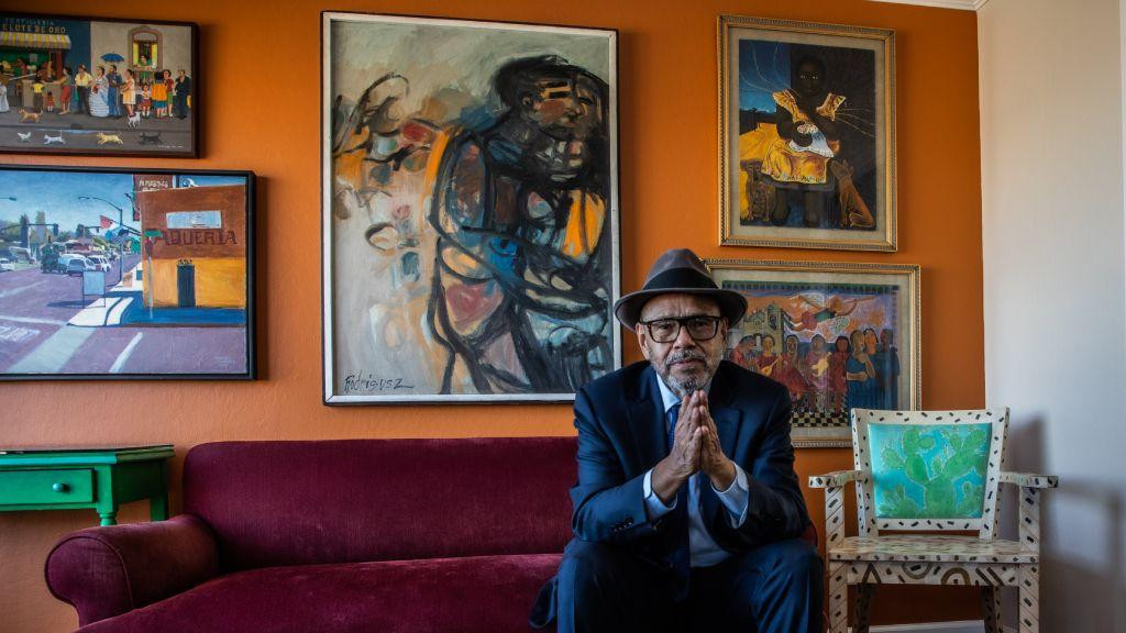 Antonio Salazar-Hobson sedi na sofi, stariji čovek u odelu i sa šeširom sedi na sofi i gleda u kameru