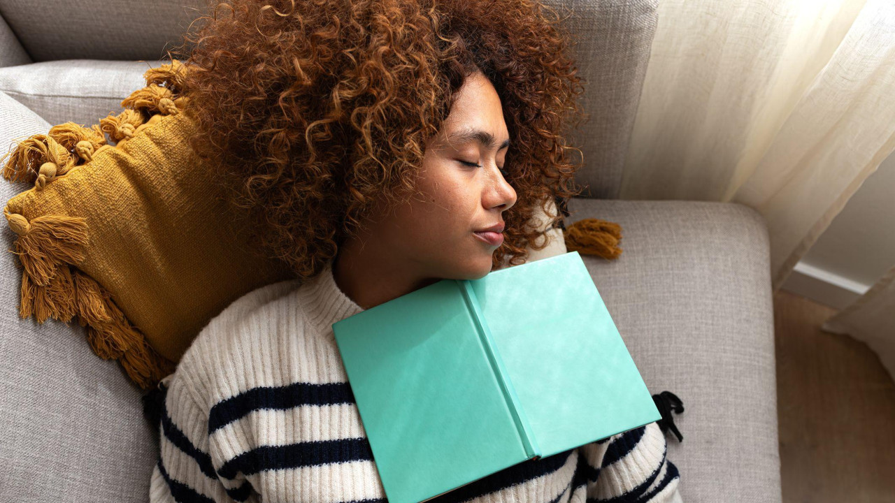 žena sa kovrdžavom kosom spava na krevetu, a preko nje je otvorena knjiga