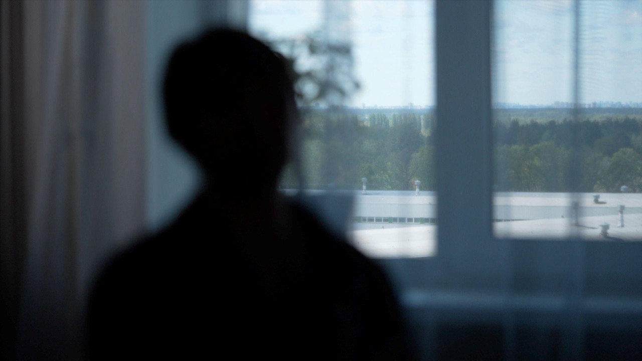 Ženska silueta gleda ka prozoru sa pogledom na zeleno drveće