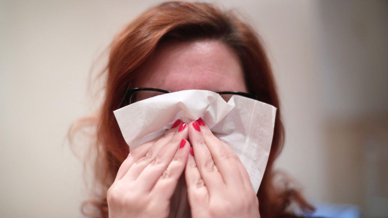Prehlađena crvenkosa žena drži maramicu ispred nosa