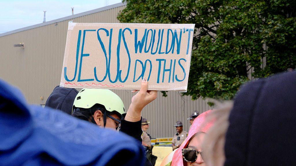 Demonstrant drži transparent sa porukom „Isus ovo ne bi uradio“ tokom protesta ispred pritvornog centra američke Imigracione i carinske službe (ICE) u Brodviewu, savezna država Ilinois, protiv najnovijeg pooštravanja imigracione politike SAD, 10. oktobra 2025. godine.