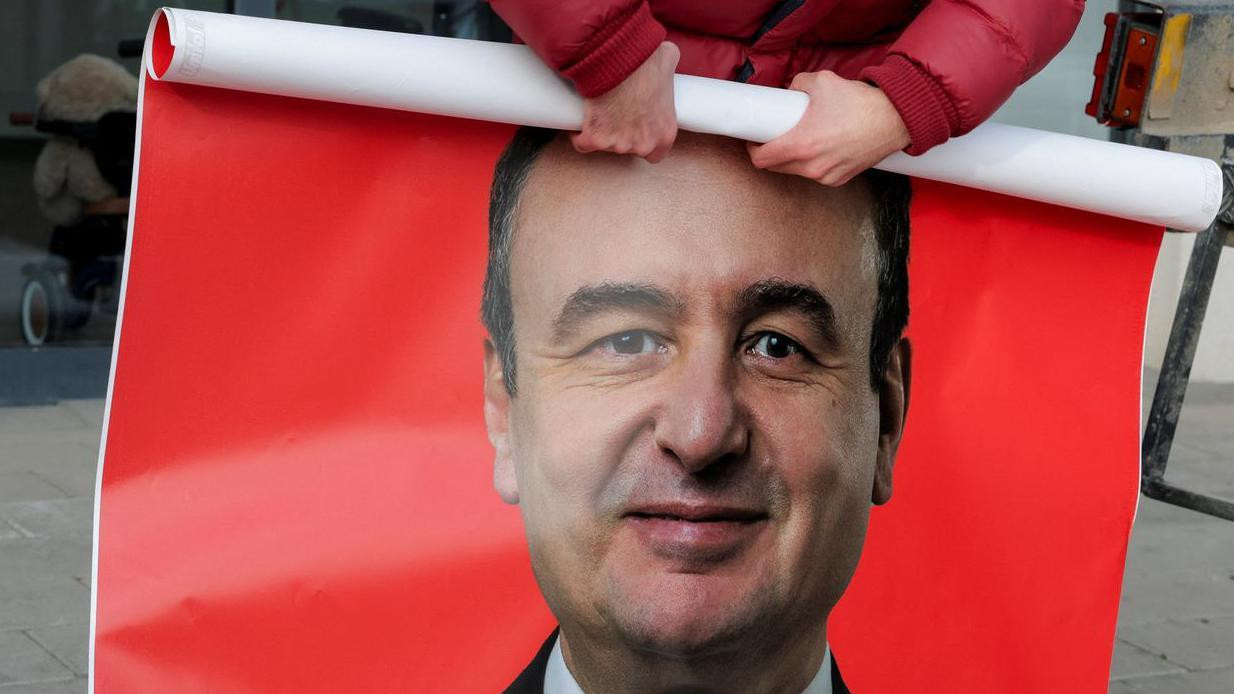 Muškarac savija poster crvene boje na kojem je lik Aljbina Kurtija