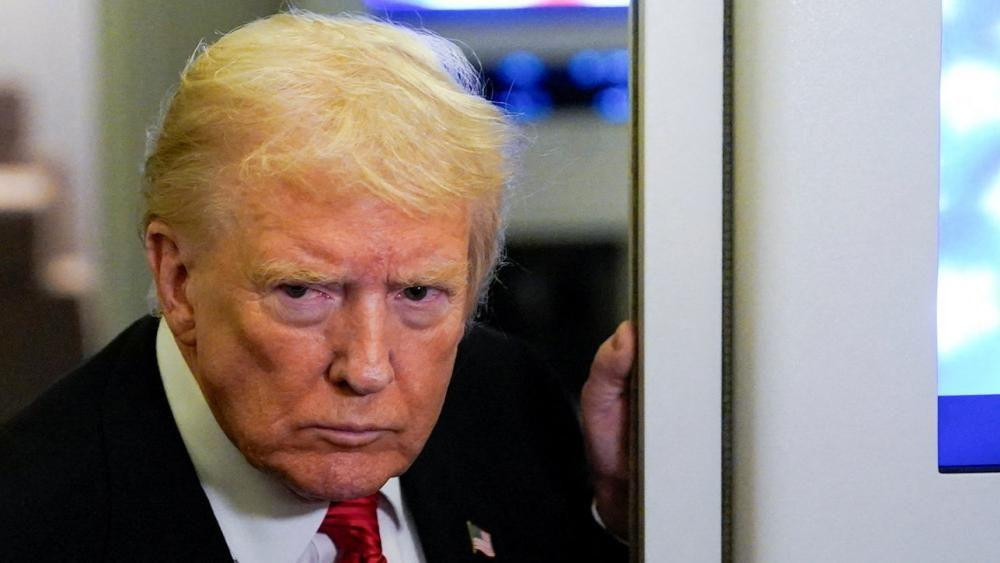 US President Donald Trump looks on as he speaks to members of the media on board Air Force One.