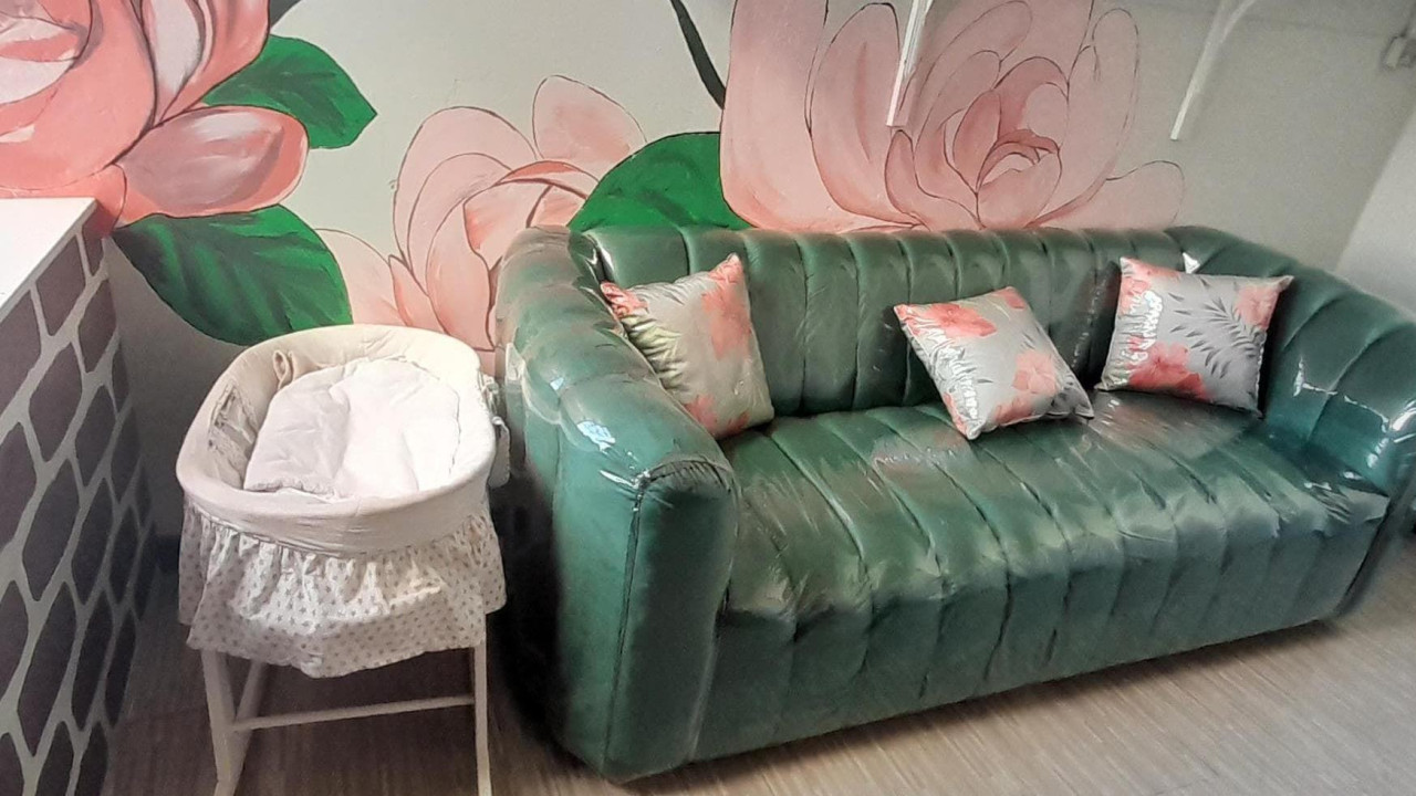 Zelena sofa i krevetac u uglu. Na zidu oslikane ruže. Soba za tugovanje