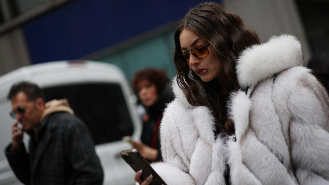 devojka u beloj bundi u ruci drži mobilni telefon 