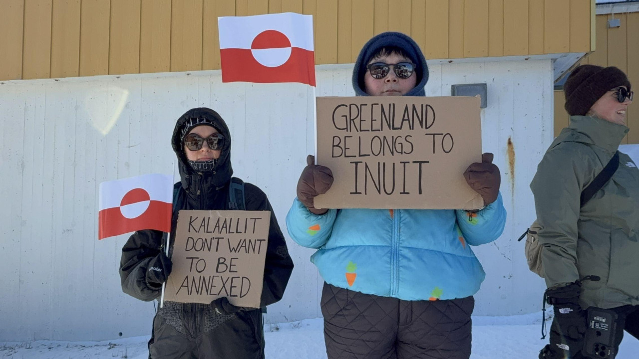 Dve žene na antiameričkom protestu na Grenlandu. Drže crveno-bele zastave starosedelaca i transparente na kojima piše „Kalalit ne želi da bude anektiran“ i „Grenland pripada Inuitima“.