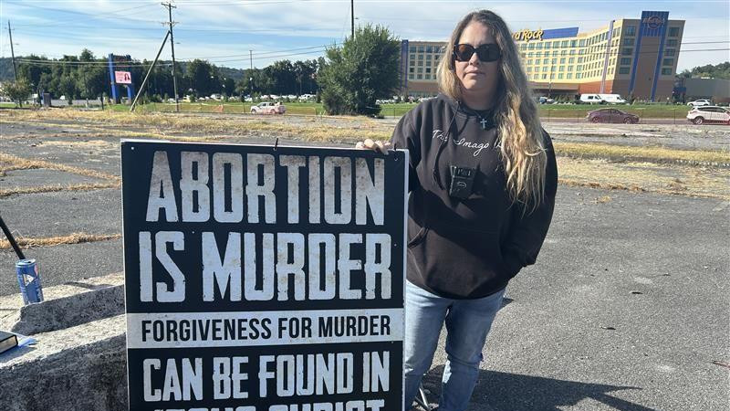 Žena u crnoj dukserici stoji ispred znaka na kojem je ispisano: Abortus je ubistvo oproštaj za ubistvo može da da samo Isus Hrist