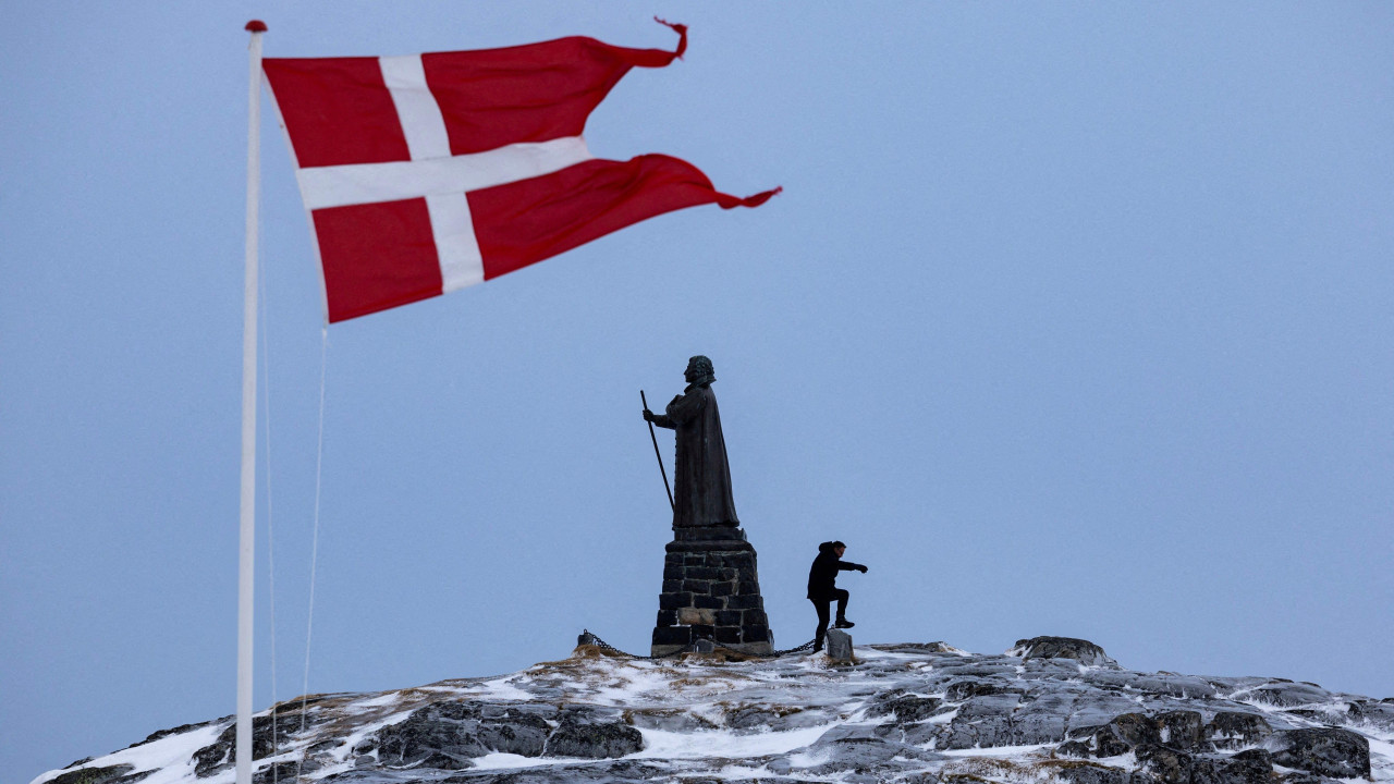 A man walks as Danish flag flutters next to Hans Egede Statue in Nuuk
