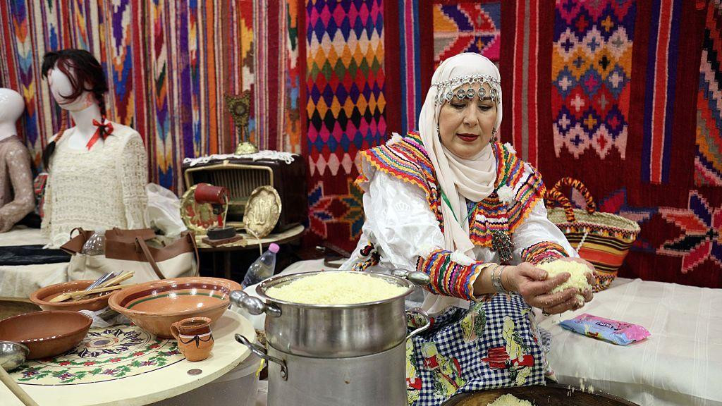 Žena, obučena u šarenu odeću, pravi kuskus