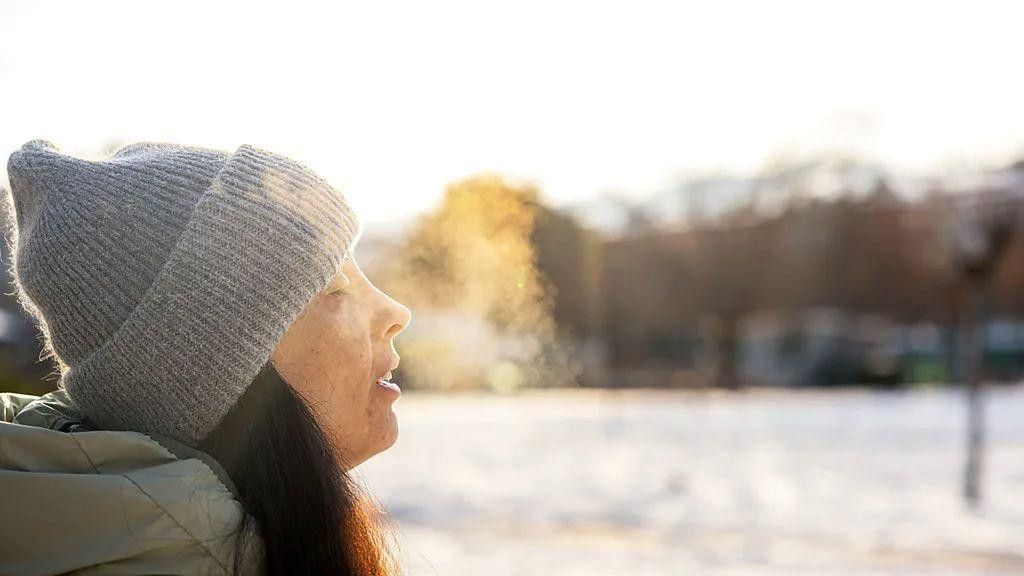 žena u kapi i zimskoj jakni diše dok se vidi vazduh koji izlazi na usta