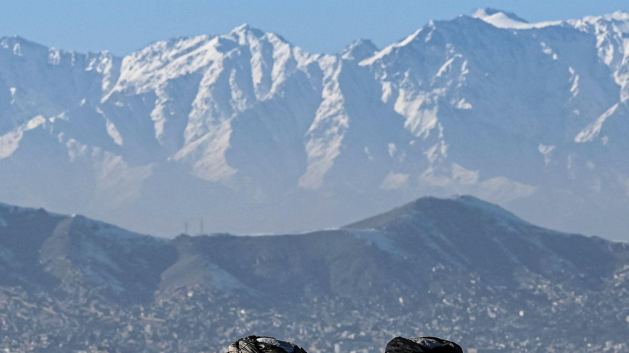 dva pripadnika talibana sede i gledaju na grad Kabul sa planinama u pozadini, okrenuti leđima kameri, snimljena na brdu Vazir Akbar Kan u januaru 2022. godine.