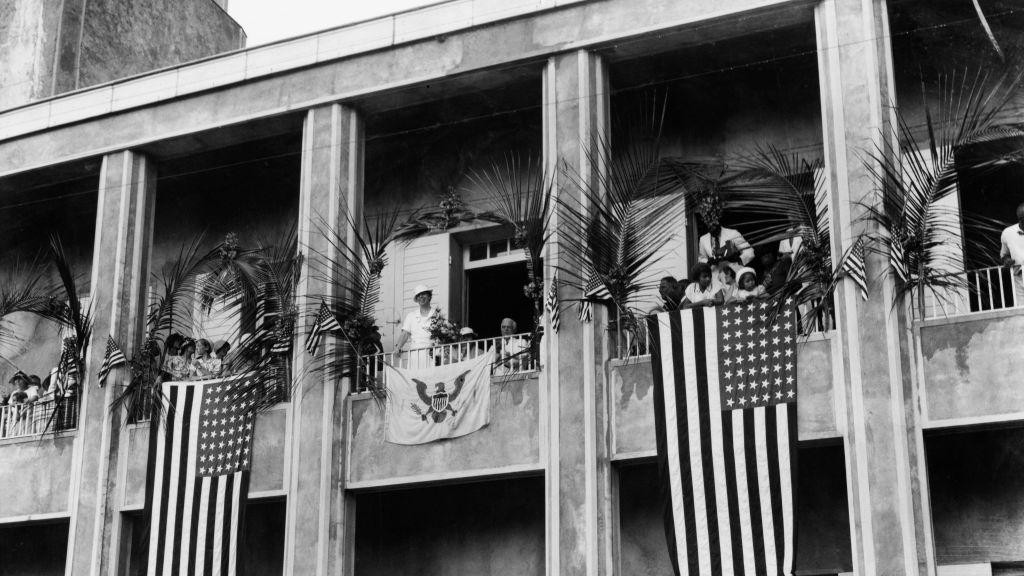 Crno-bela fotografija fasade zgrade Svetog Tome sa velikim američkim zastavama koje vise sa njenih balkona. Eleonor Ruzvelt, tada prva dama SAD, je na jednom od balkona, na slici iz 1934. godine.