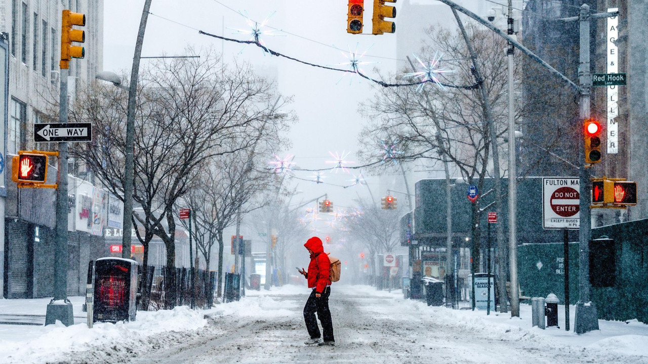 muškarac u crvenoj jakni s rancem na leđima prelazi ulicu