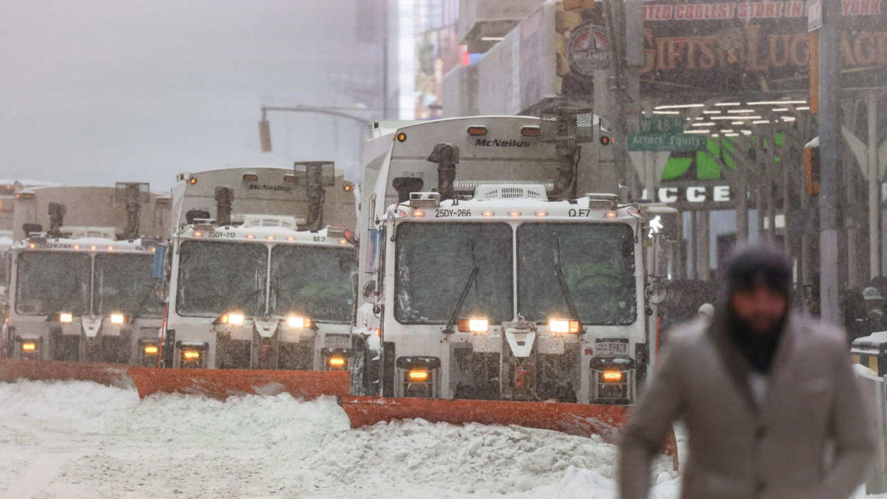 U prvom planu muškarac sa kapom i šalom u sivom kaputu, u drugom planu kamioni koji čiste sneg sa ulice 