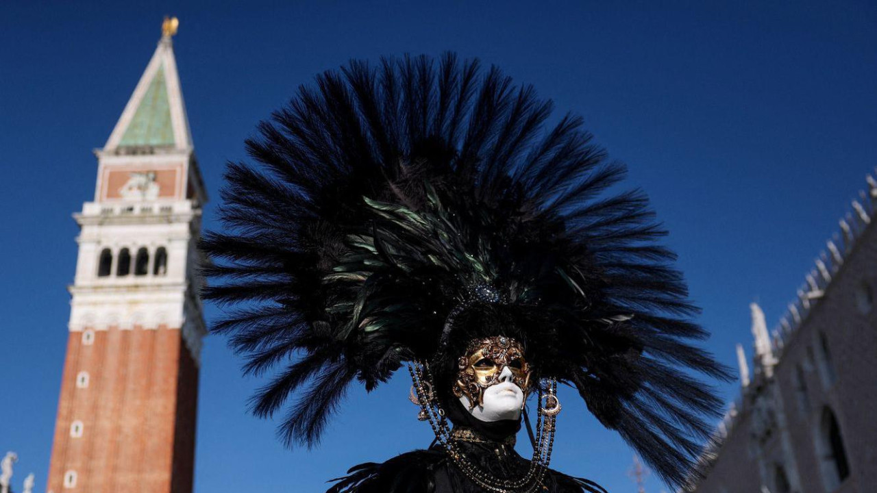 Čovek na licu ima paunovo perje iza se vidi toranj crkve Svetog Marka u Italiji