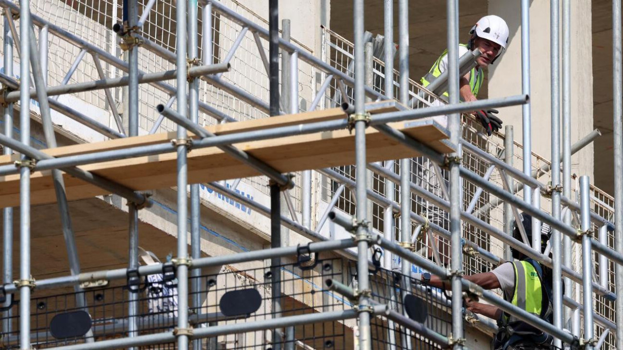 Građevinska skela i dva radnika u prslucima i sa kacigama na glavi