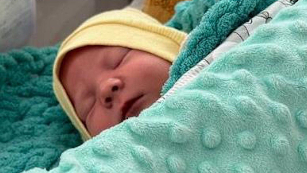 A sleeping baby in a yellow hat lies in a hospital bed in Kyiv, under a light green blanket