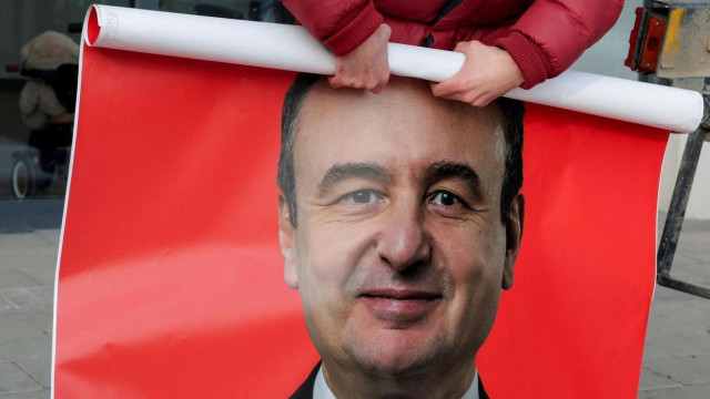 Muškarac savija poster crvene boje na kojem je lik Aljbina Kurtija